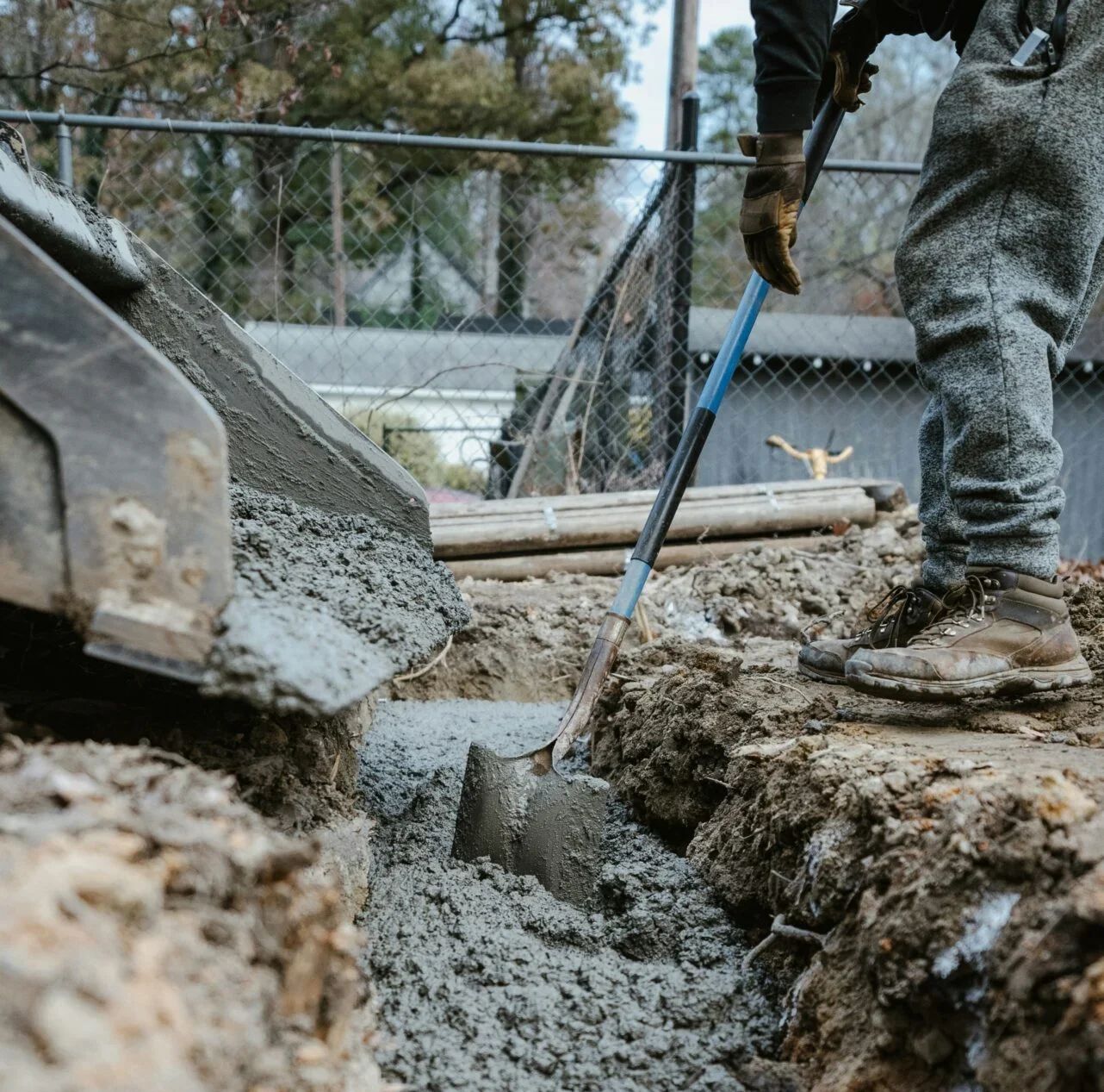Worker smoothing wet concrete in trench with shovel.